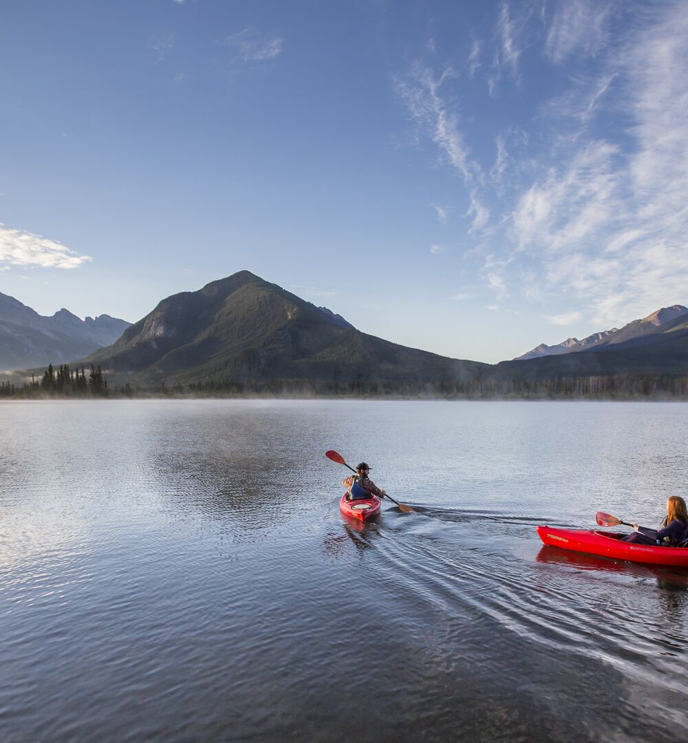 Two people in kayaks paddling on Vermilion Lakes at sunrise